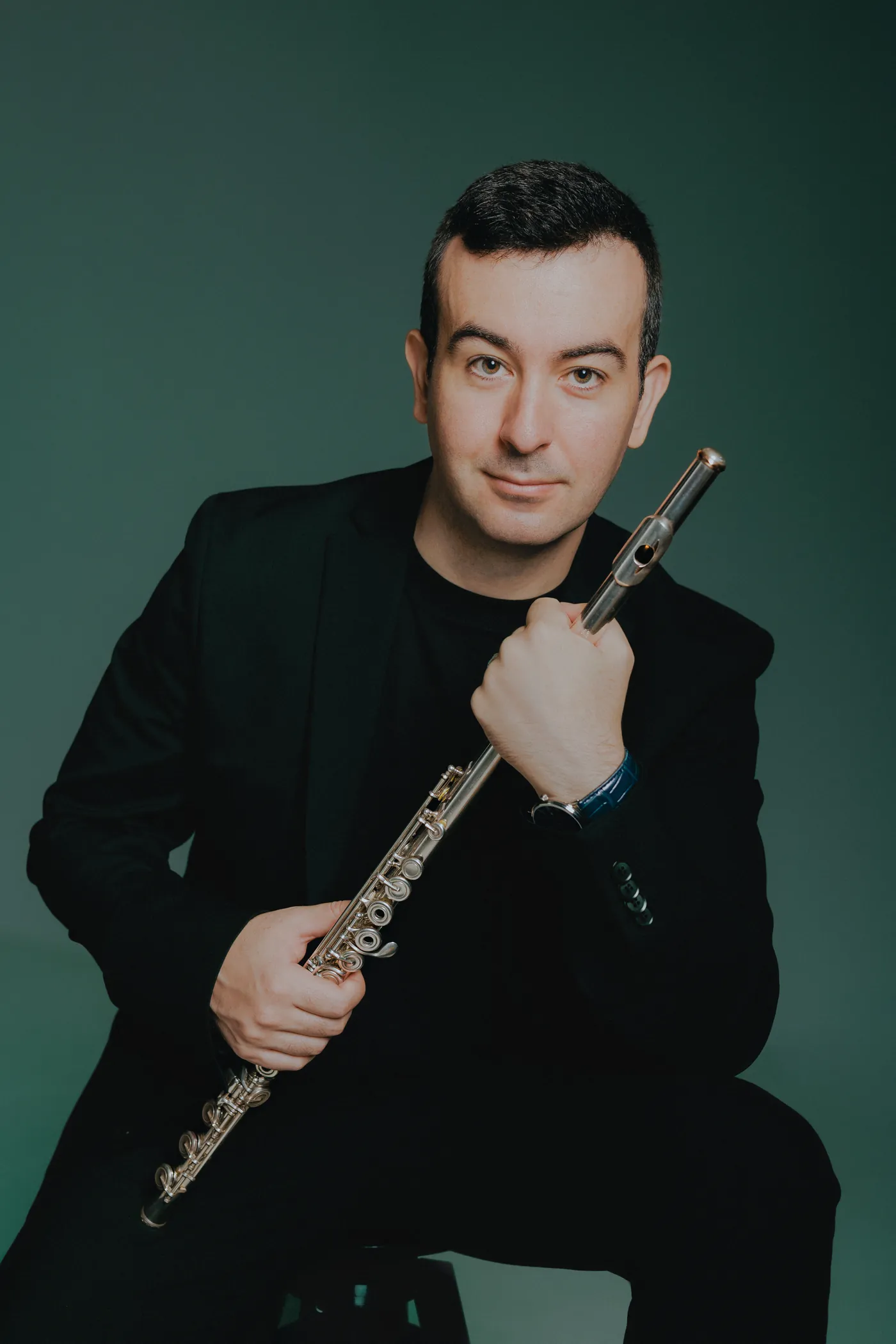 Alberto Acuña seated with his flute against a dark green background